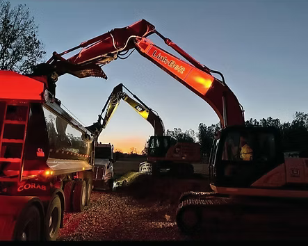 Two back hoes, one red and the other yellow, with the sunrise in the background. 